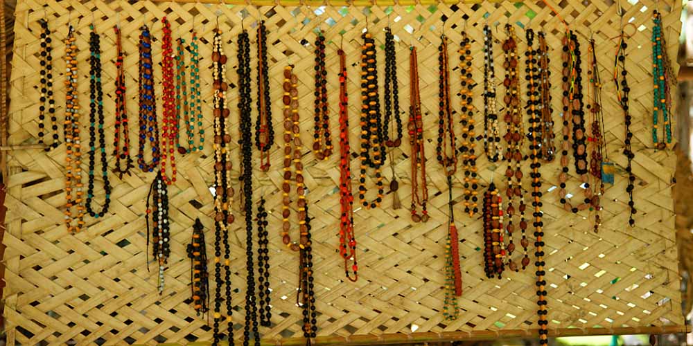 Une collection de colliers traditionnels suspendus sur un panneau en bambou tressé