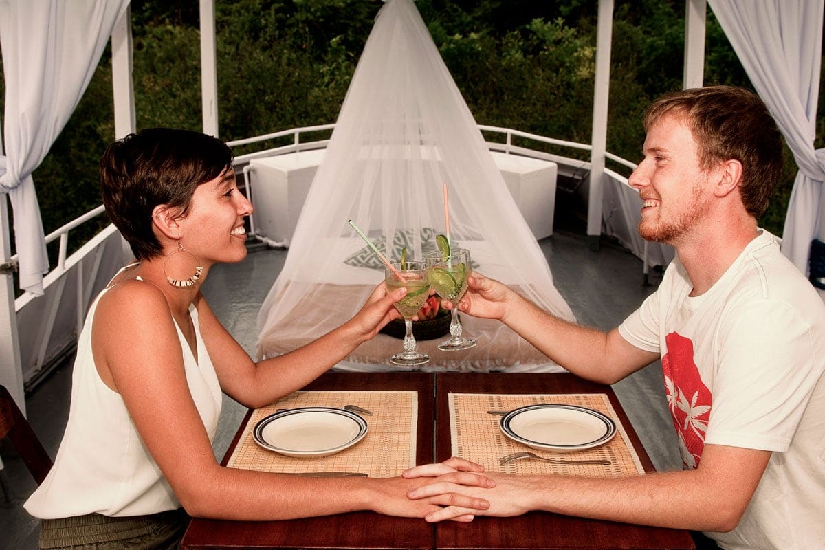 Un couple échange un toast avec des cocktails sur le pont d’un bateau en Amazonie