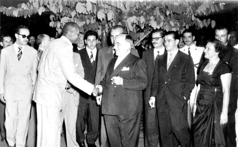 Photographie en noir et blanc montrant une rencontre historique entre Mestre Bimba, pionnier de la capoeira régionale, et le président brésilien Getúlio Vargas, dans une réception officielle.