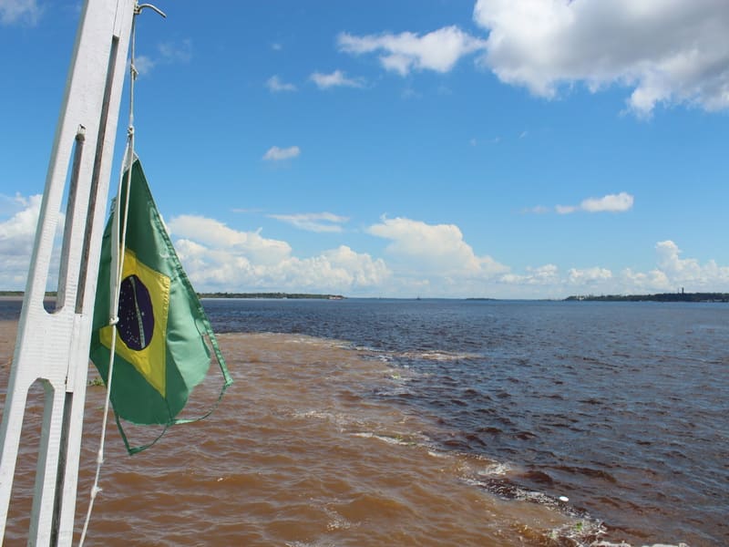 Photo prise depuis un bateau montrant le phénomène naturel de la “Rencontre des eaux” à Manaus, où les eaux sombres du Rio Negro et les eaux claires du Rio Solimões se rejoignent sans se mélanger immédiatement. 