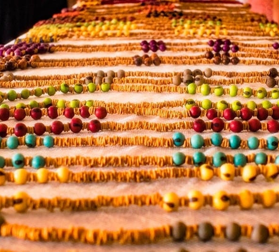 Gros plan sur une table recouverte de colliers artisanaux faits de graines naturelles colorées.