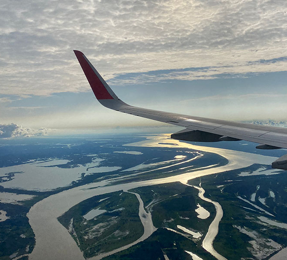 Vue depuis le hublot d’un avion en vol, montrant une large portion du fleuve Amazone serpentant entre les forêts, baignée par la lumière dorée du soleil couchant.