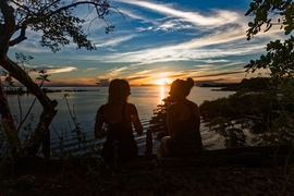 Deux personnes assises près du fleuve regardent un coucher de soleil coloré